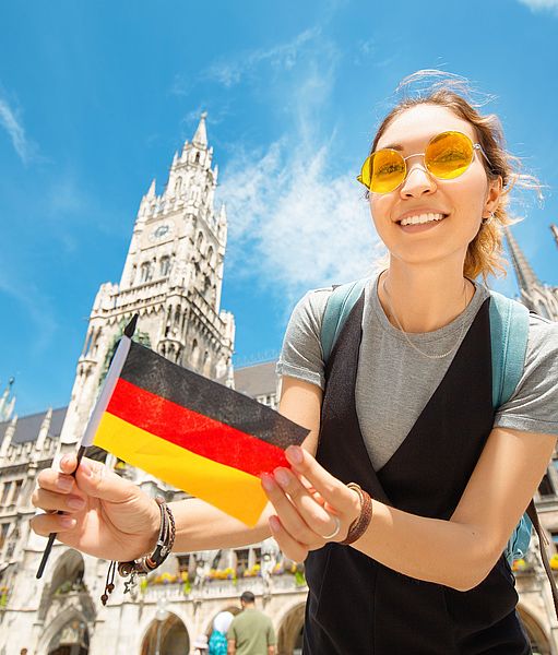 Chica estudiante internacional sonriendo con una bandera alemana en la mano en Múnich